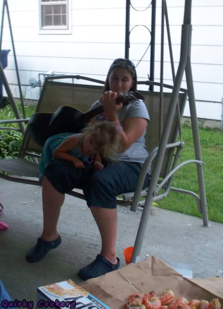 Kid climbing onto her mom's lap while she's playing the guitar