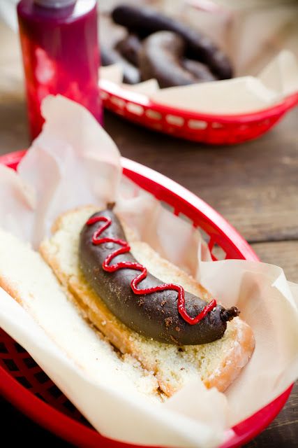 Cupcake cake that looks like a hot dog or sausage bratwurst on a long john doughnut bun and raspberry icing as ketchup