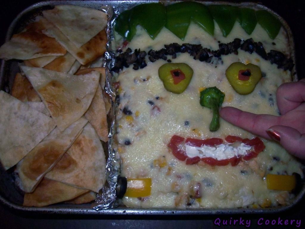 Frankestein casserole with cheese face, pepper bolts, pepper hair, olive scar and hair, pickles for eyes, pepper stem nose