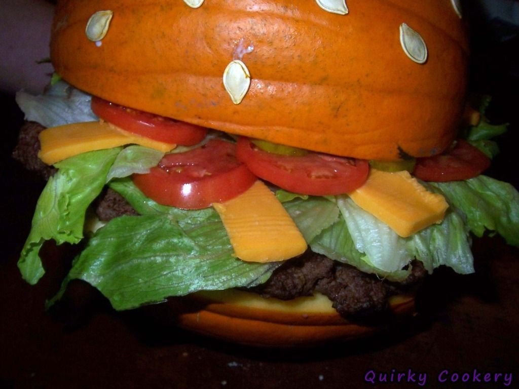 Giant fake burger made out of a whole pumpkin to look like the bun with a large burger patty and toppings inside. Pumpkin seeds glued to the outside to look like a sesame seed bun. 