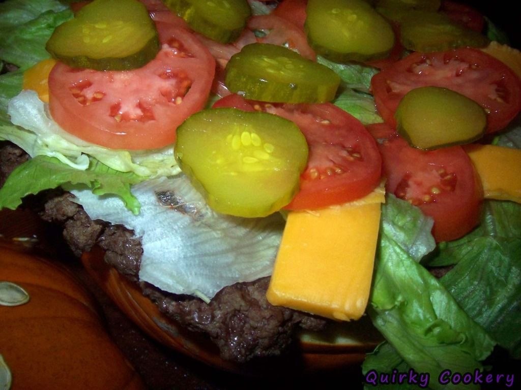 Giant fake burger made out of a whole pumpkin to look like the bun with a large burger patty and toppings inside. Pumpkin seeds glued to the outside to look like a sesame seed bun. 