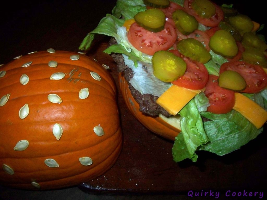 Giant fake burger made out of a whole pumpkin to look like the bun with a large burger patty and toppings inside. Pumpkin seeds glued to the outside to look like a sesame seed bun. 