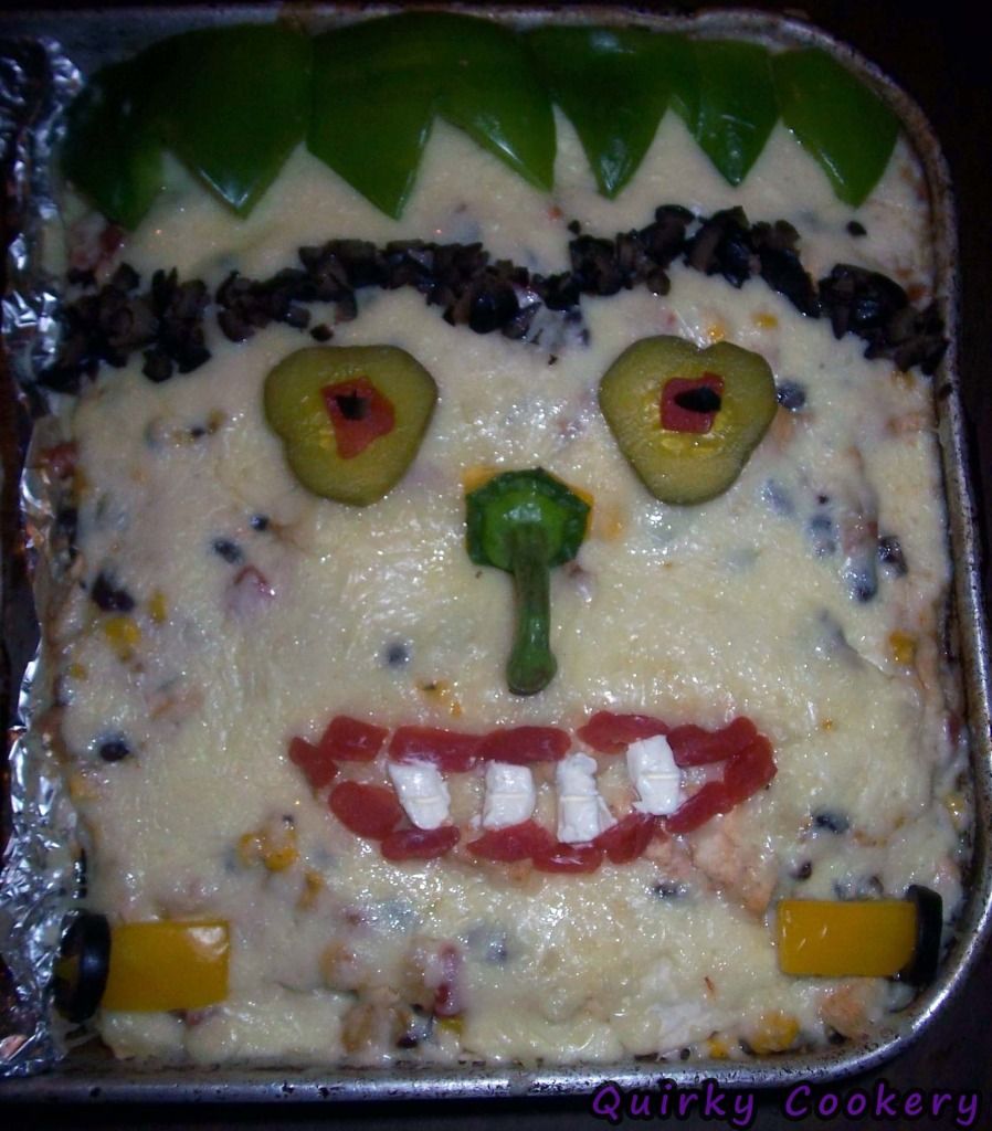 Frankestein casserole with cheese face, pepper bolts, pepper hair, sliced black olives scar and hair, pickles for eyes, pepper stem nose