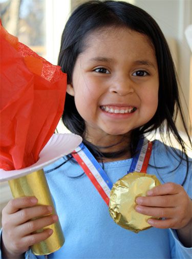 Little girl posing with Olympics torch made of paper plate, toilet paper roll covered in gold foil, red tissue paper flame - Gold medal with cookie covered in foil