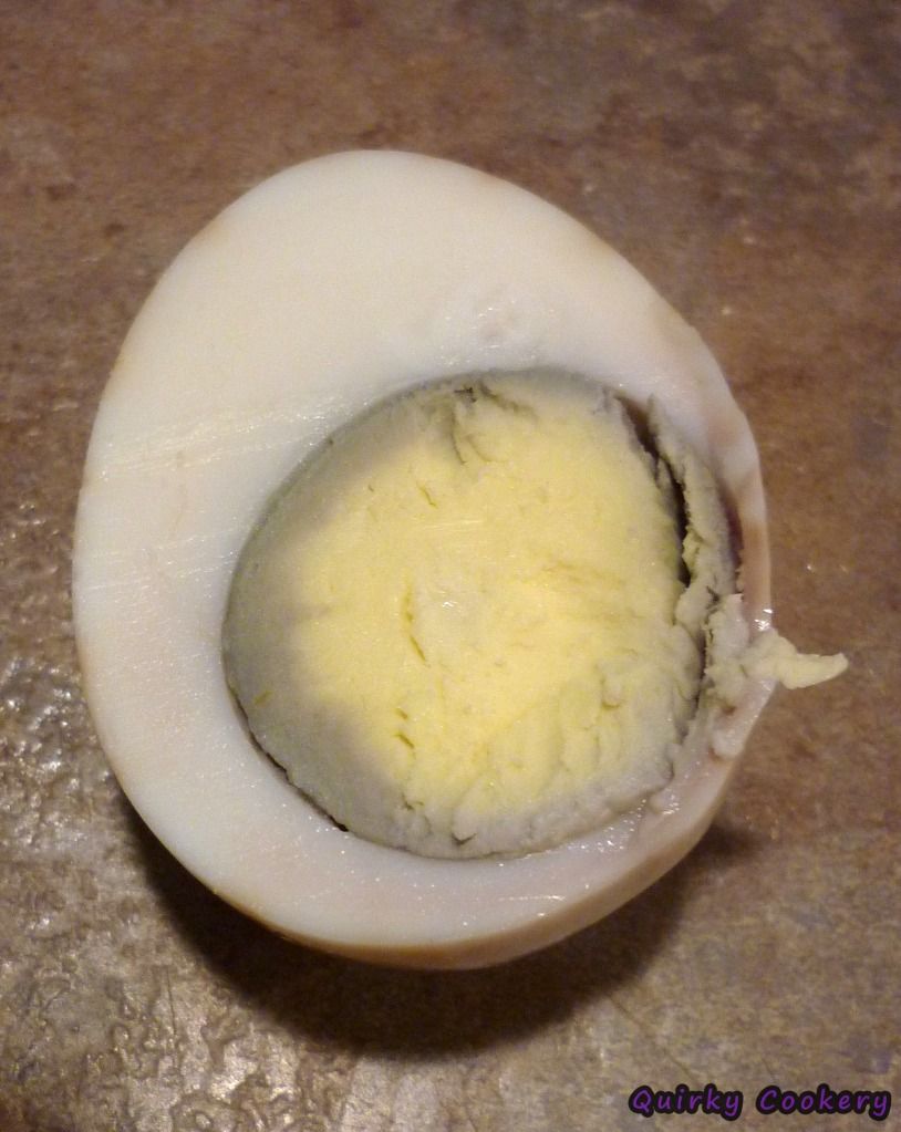 Boiled egg sliced open. The yolk is dark grey from being overcooked. The outer white is marbled with tea. 